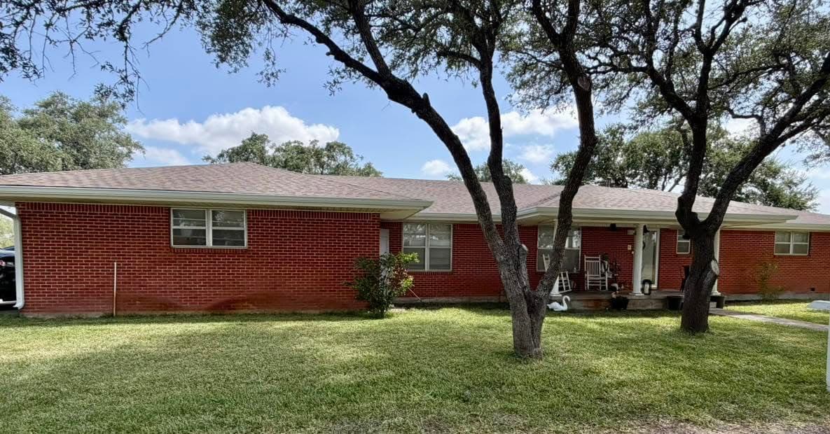 Red brick ranch home under live oaks with white seamless gutters