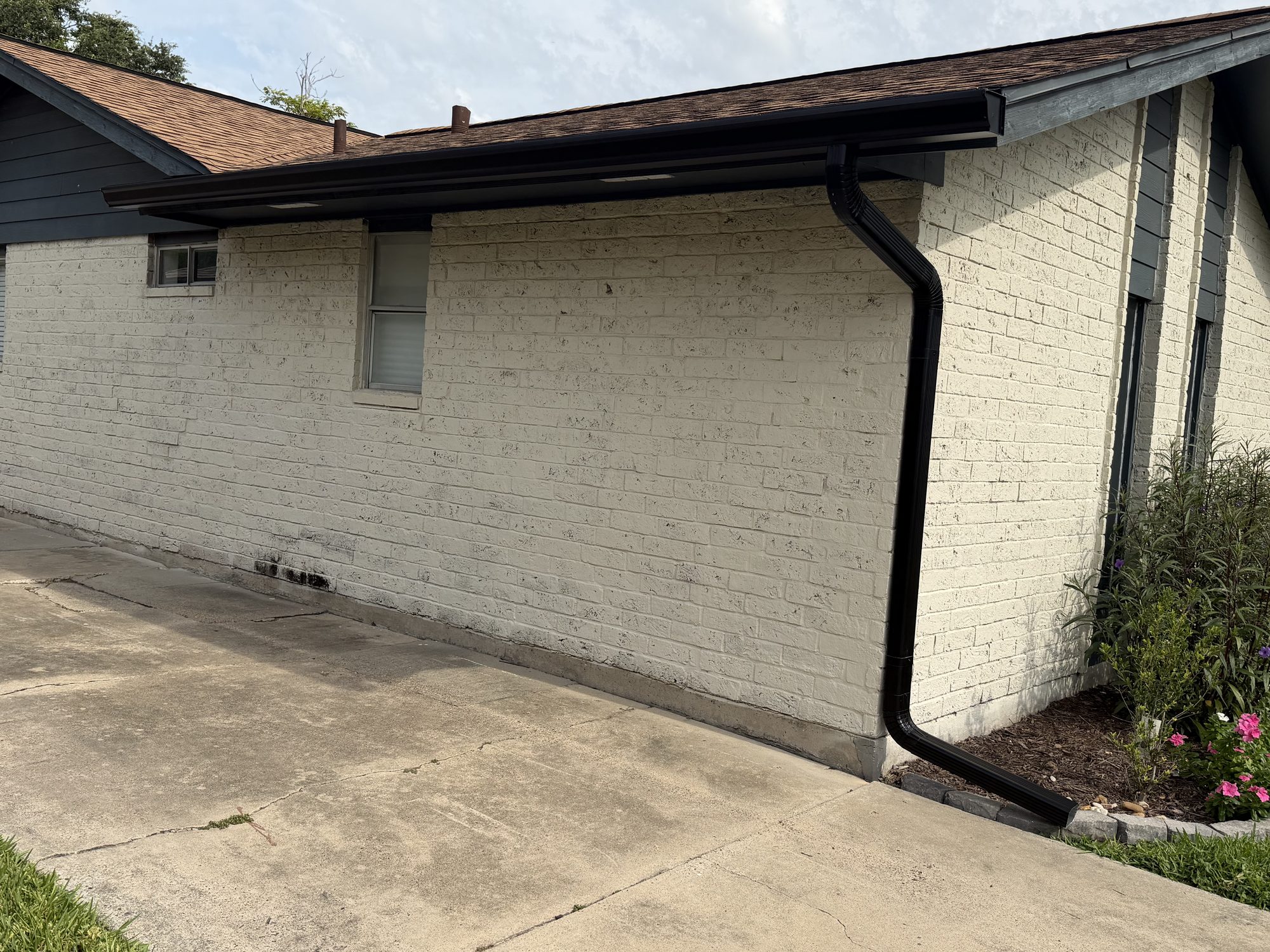 Black seamless gutter and full downspout run on white brick in Portland by J Seamless Gutters