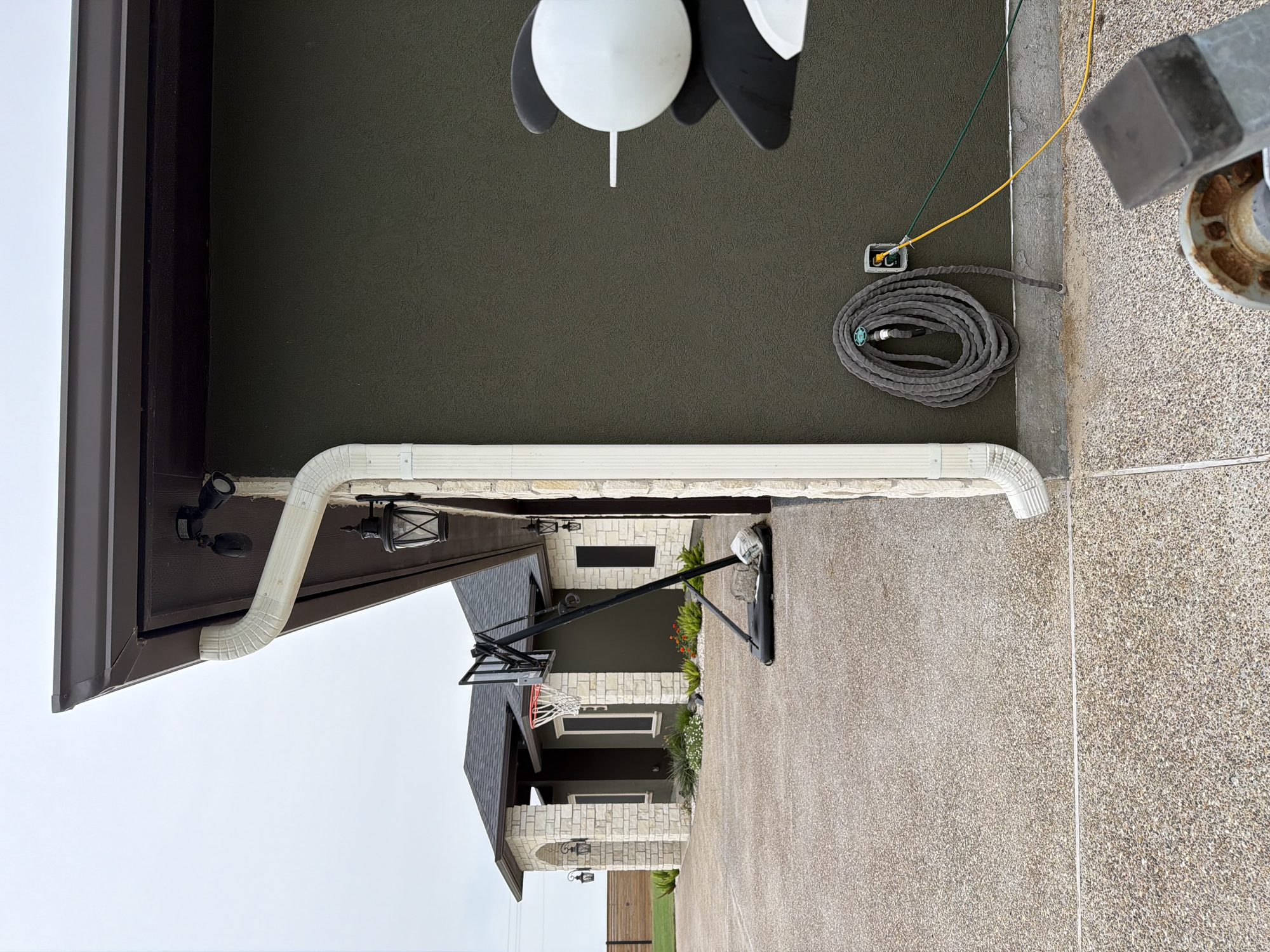 White downspout and seamless eave on a dark stucco Coastal Bend house